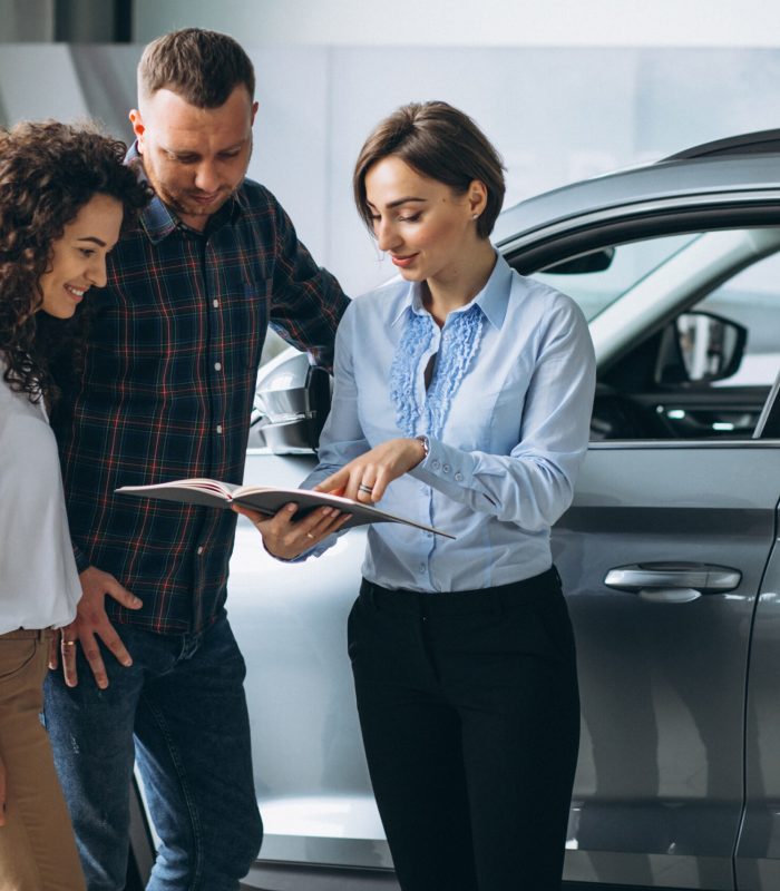 Young couple talking to a sales person in a car showroom